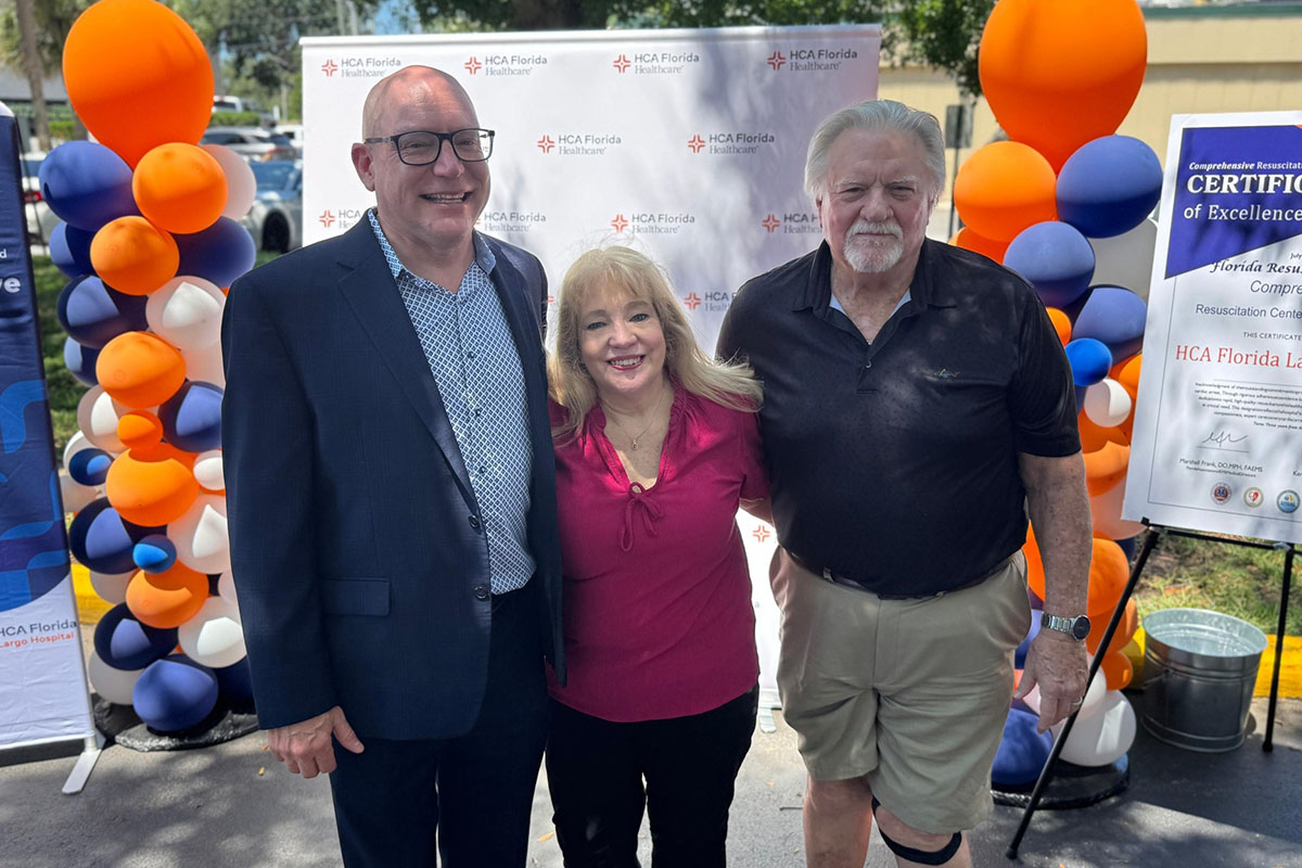 Two men and a woman smiling with orange, blue, and white balloons in the background