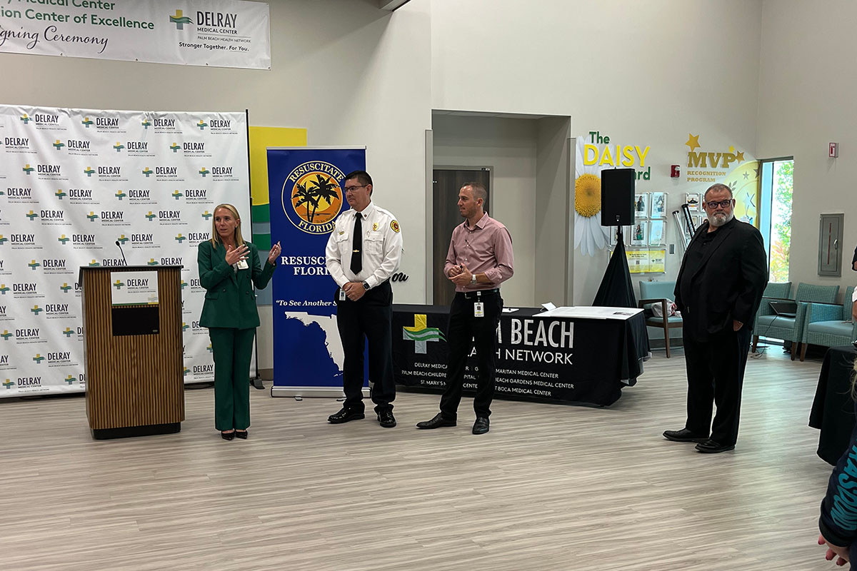 A woman talking to three men with a Resuscitate Florida banner in the background